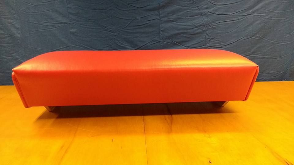 Orange rectangular cushioned bench on a wooden surface against a dark backdrop