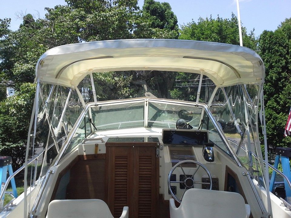 Covered boat deck with steering wheel and tan seating, docked outdoors near trees.