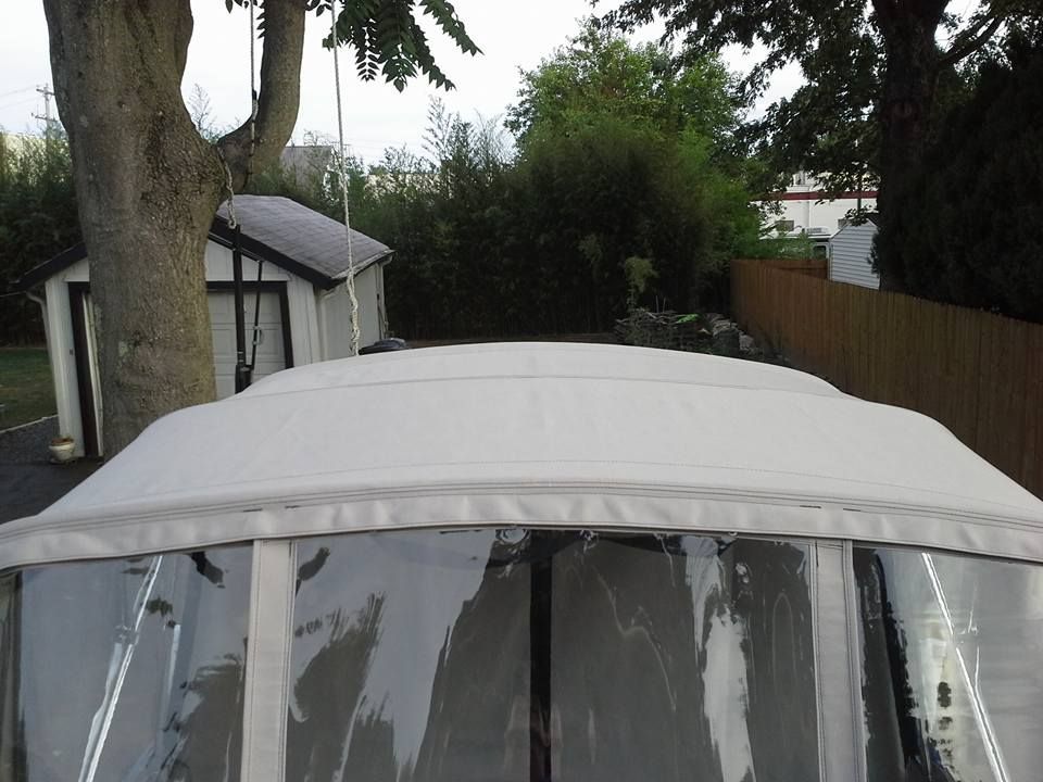 White canopy over a boat in a backyard, with trees and a shed in the background