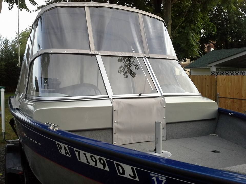 Small motorboat with a gray canopy moored beside a wooden fence and trees