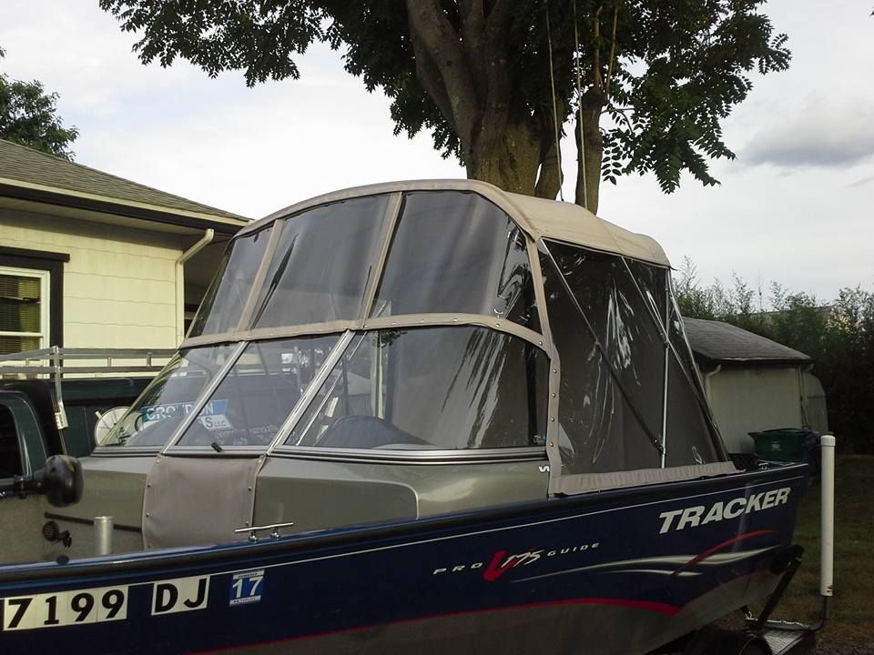 Blue Tracker boat with a clear vinyl canopy parked beside a house under trees