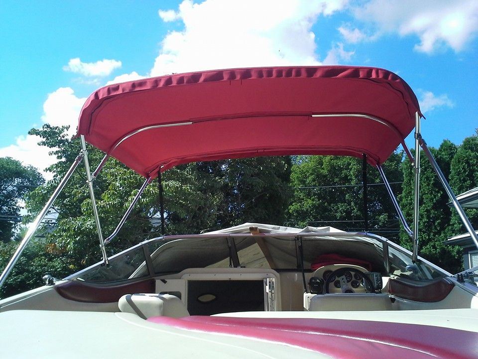Red boat canopy over a small boat on the water, with green trees and blue sky in the background