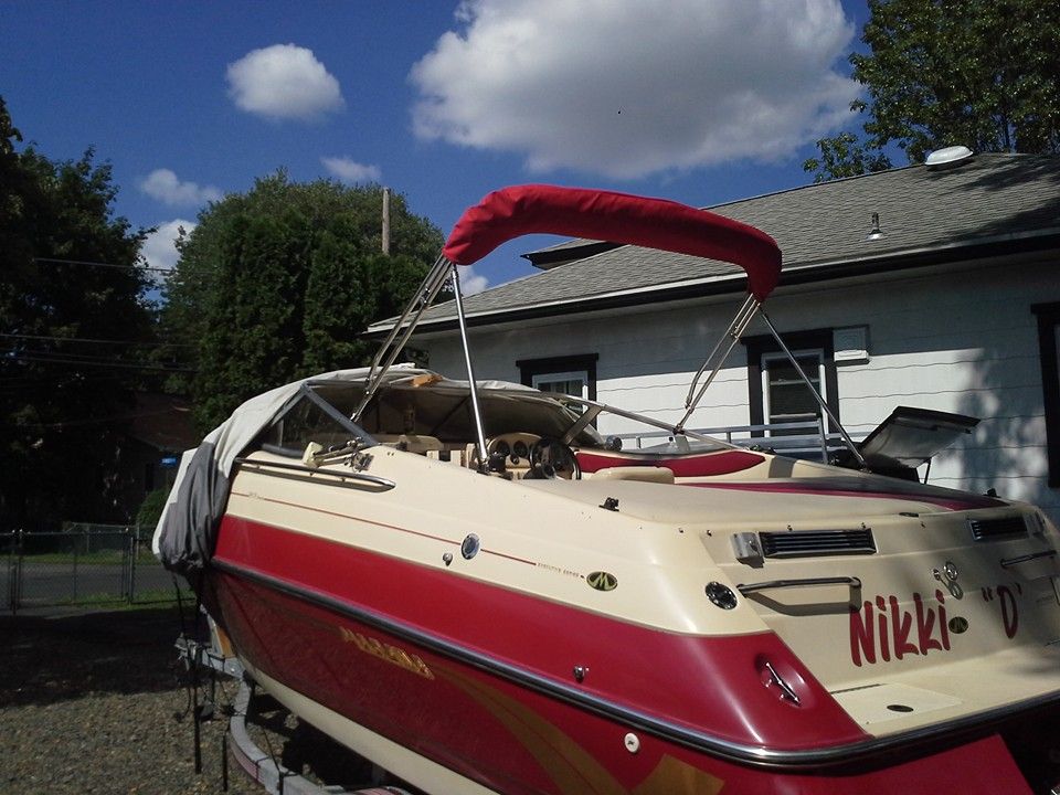 Red and cream speedboat with a red canopy parked on a driveway beside a house, under a blue sky