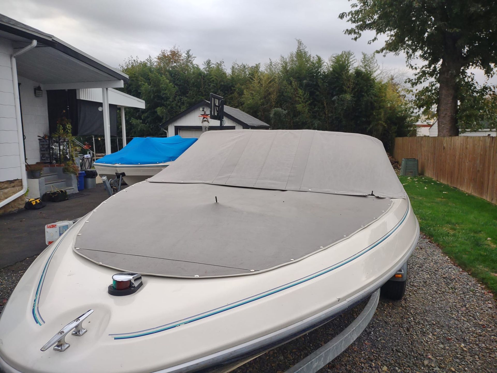 White speedboat with gray cover parked on gravel beside a house and wooden fence
