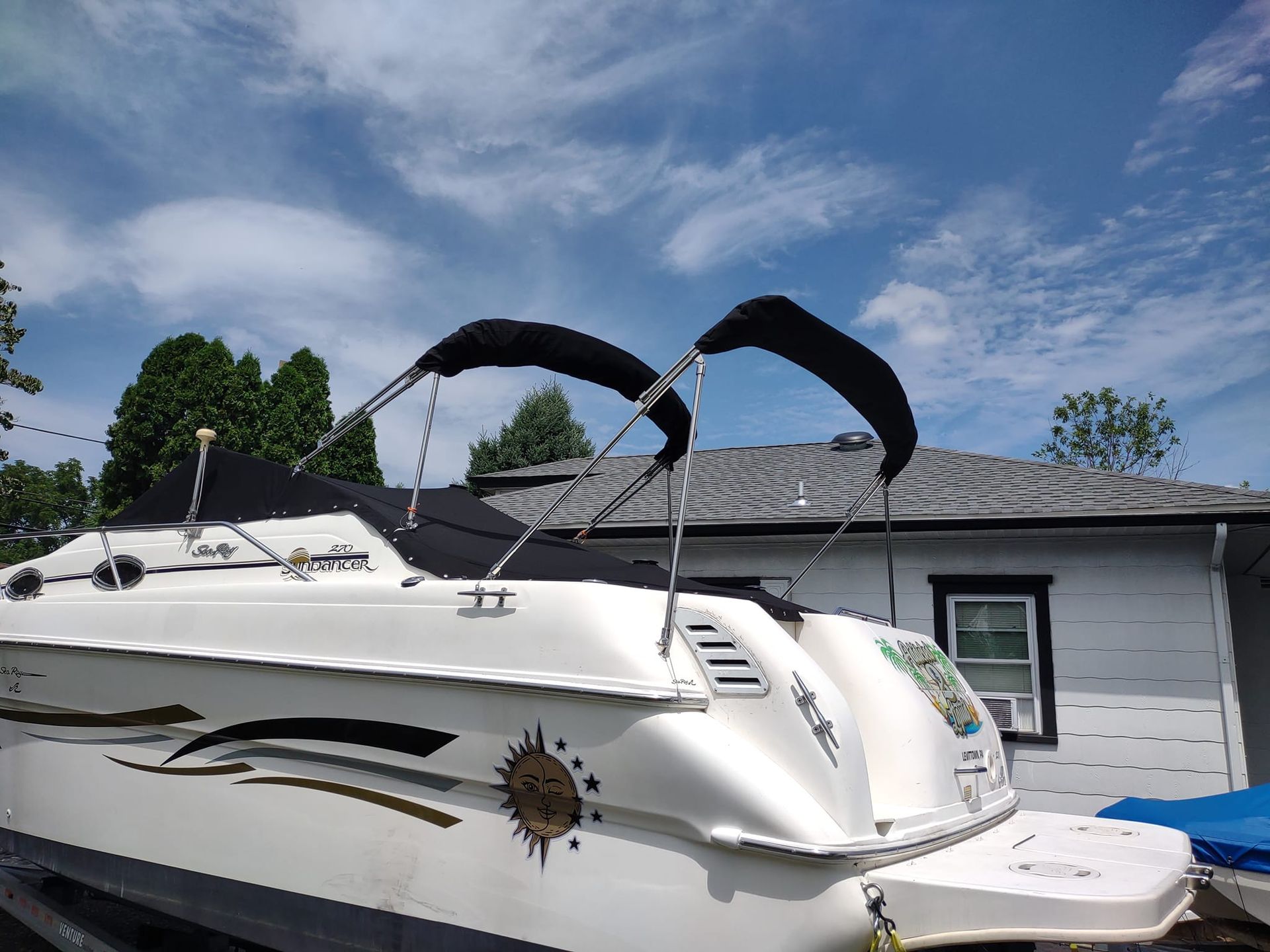White yacht on a trailer parked beside a house under a blue sky