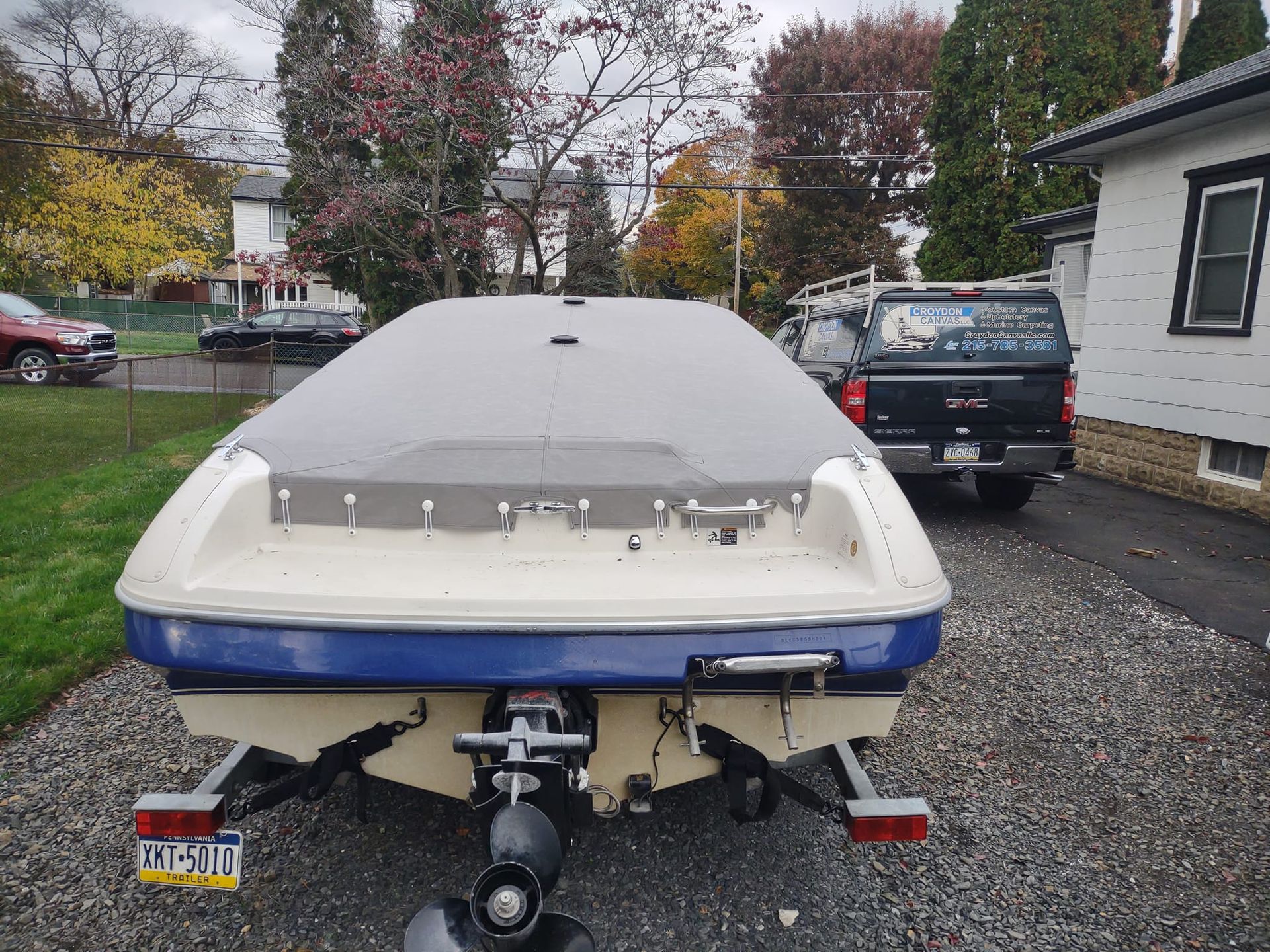 Small speedboat on a trailer parked in a gravel driveway, rear view on a cloudy day