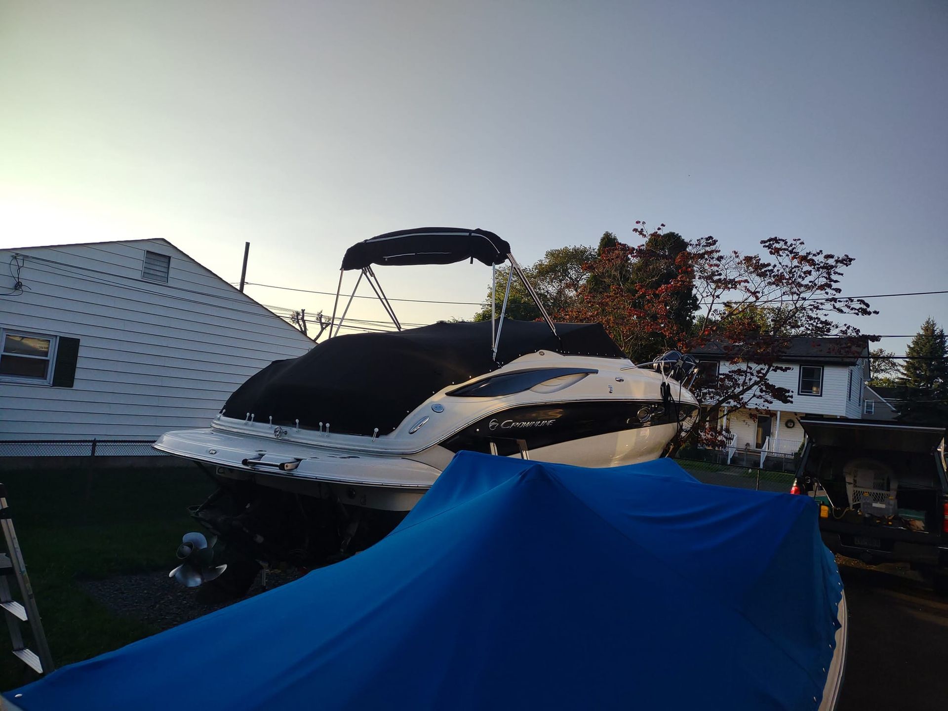 Blue-covered boat in a yard with a black-and-white yacht behind it at sunset