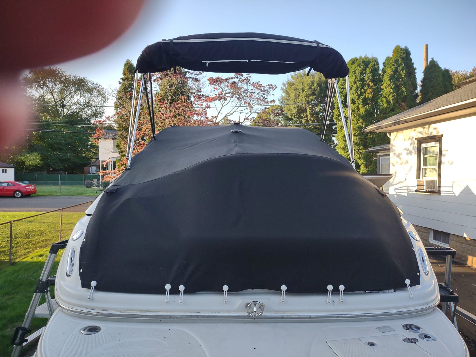 Boat with a black canopy cover on a trailer, seen from the rear in a driveway