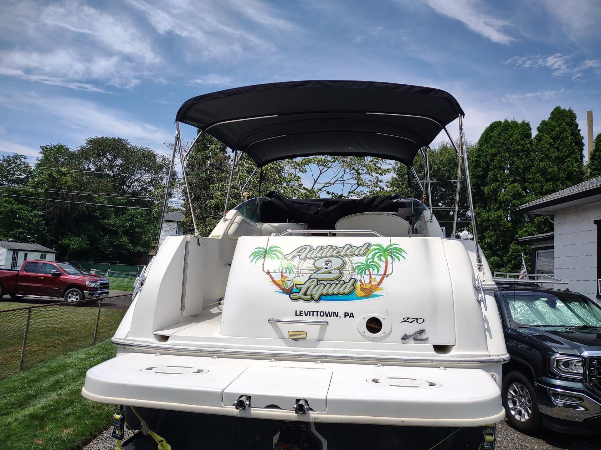 White boat with black canopy parked outdoors on a trailer, with colorful rear decal and trees in the background