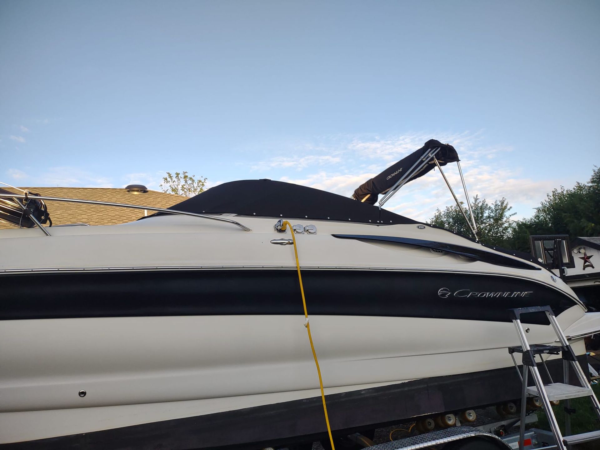 White boat on a trailer with a yellow strap, outdoor yard, and a ladder on the right