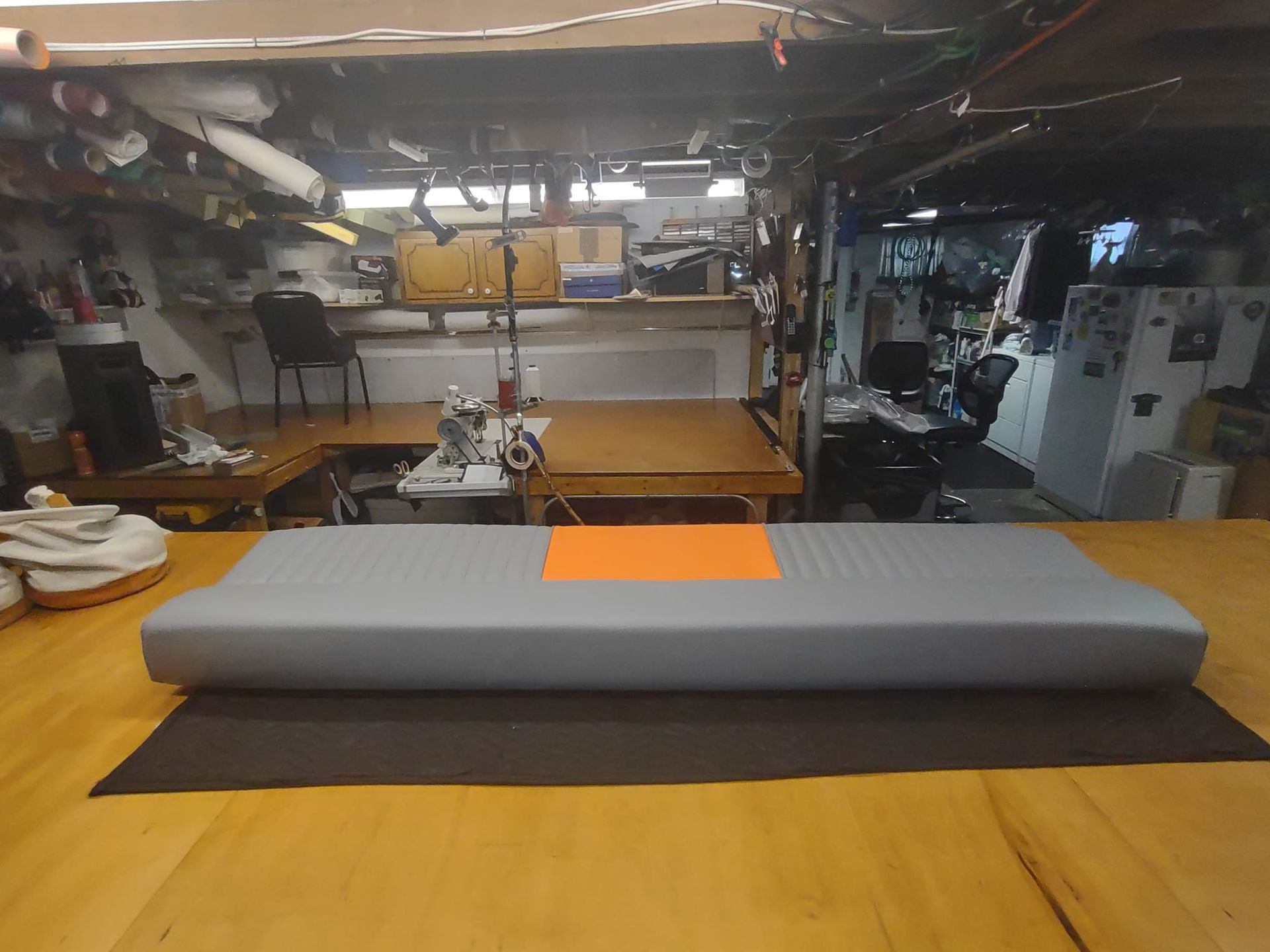 Workshop with a long gray cylindrical cushion on a black mat, tools and equipment in the background.
