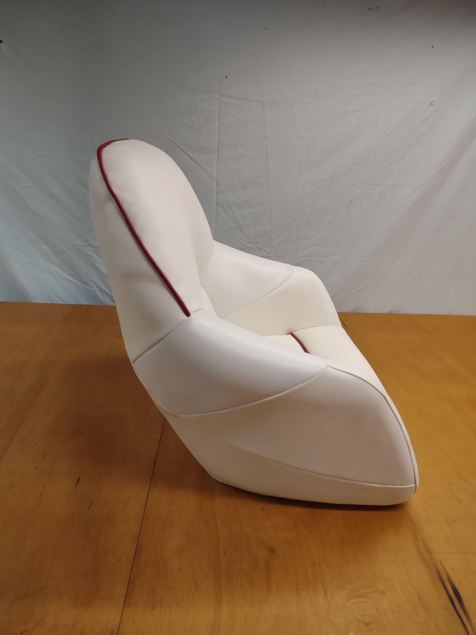 White padded chair with red trim on a wooden floor against a gray backdrop