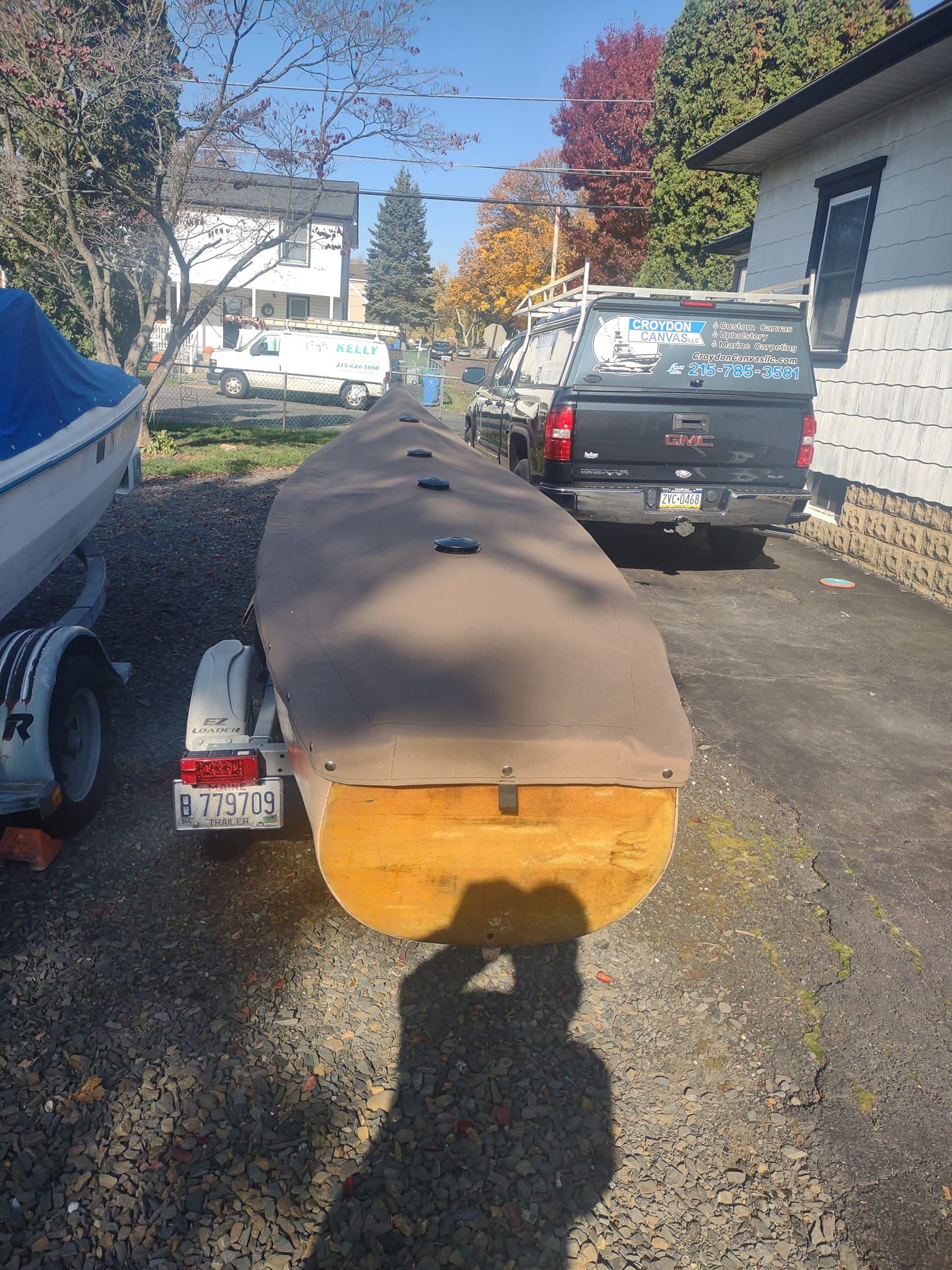 Upside-down canoe hull in a driveway, with trucks and autumn trees in the background.