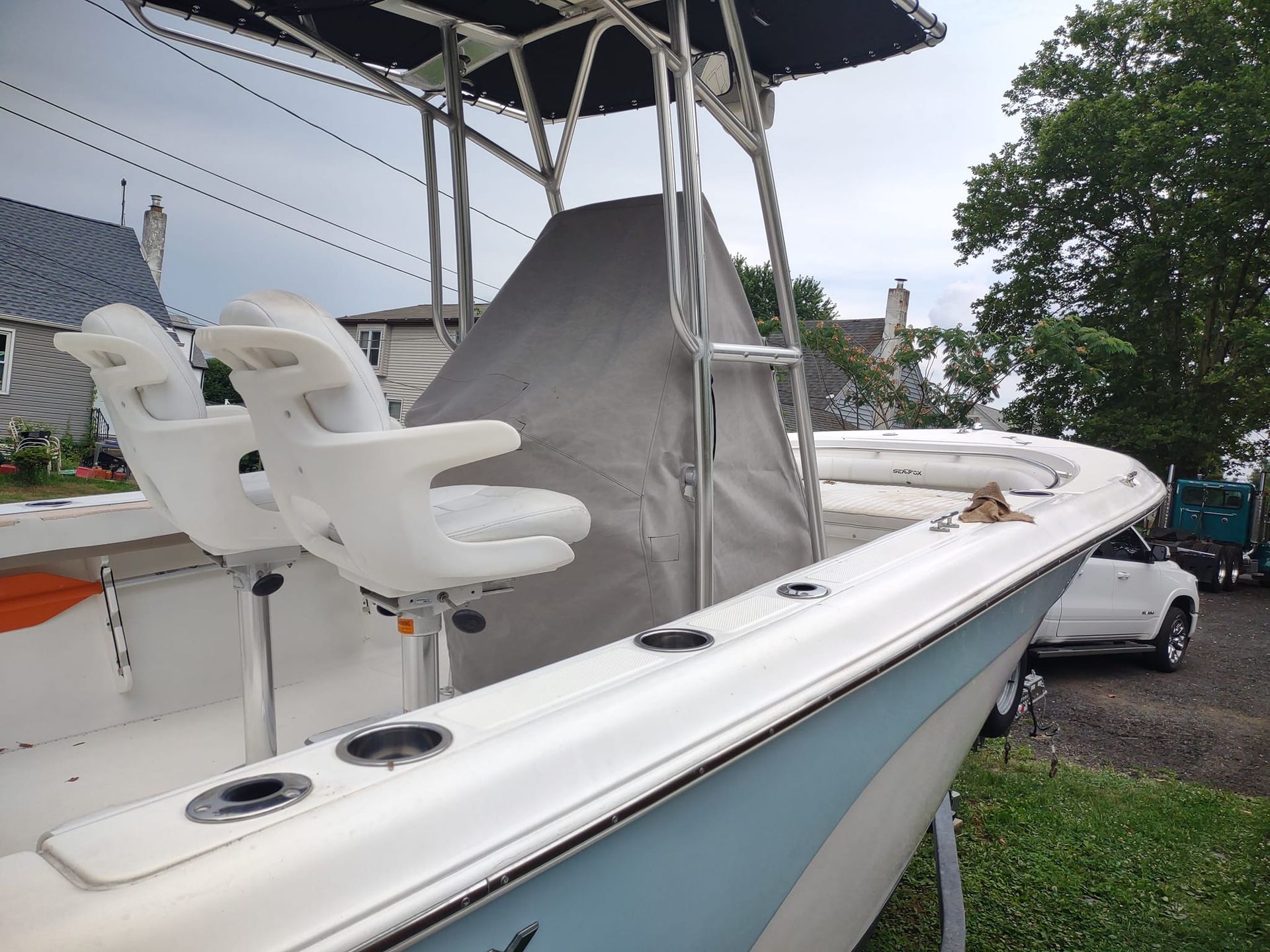 White fishing boat with twin seats docked beside grass and a car under an overcast sky