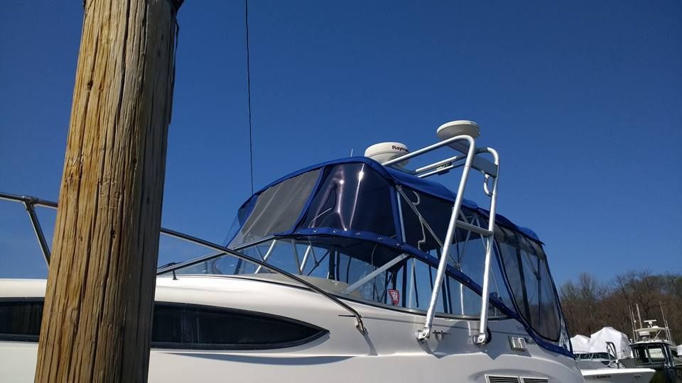White yacht with blue canopy and metal railings docked beside a wooden post under a clear blue sky