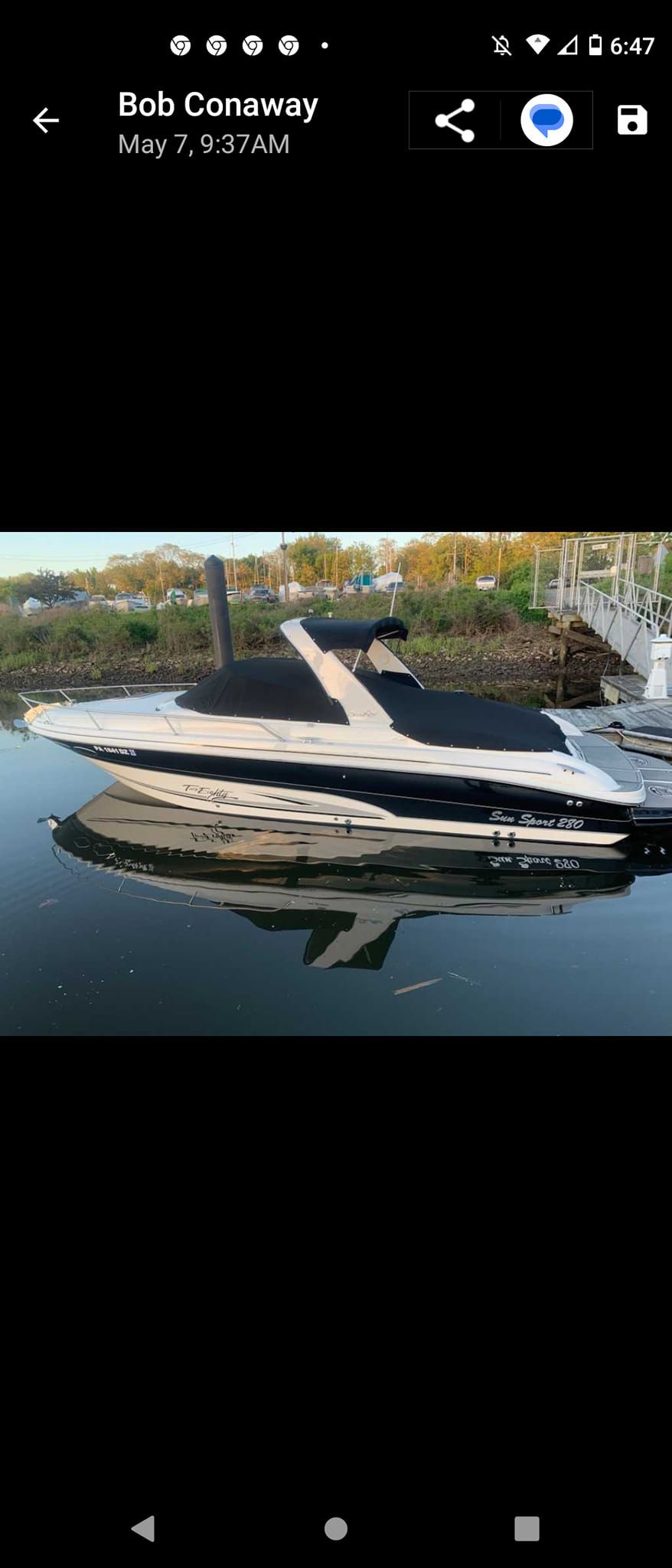 Black-and-white yacht moored on calm water near a wooded shoreline, viewed from the side.