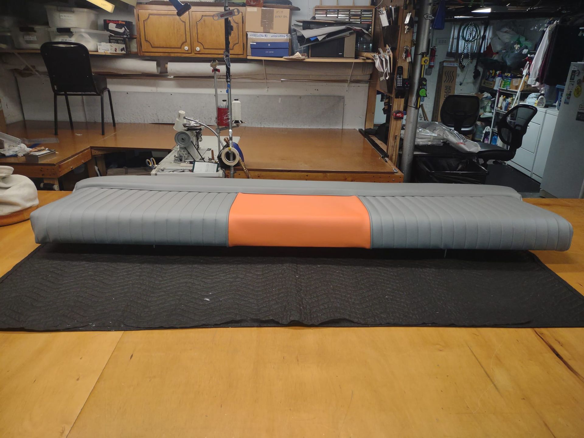 Grey and orange bolster cushion on a mat in a workshop with sewing machine and wooden worktables