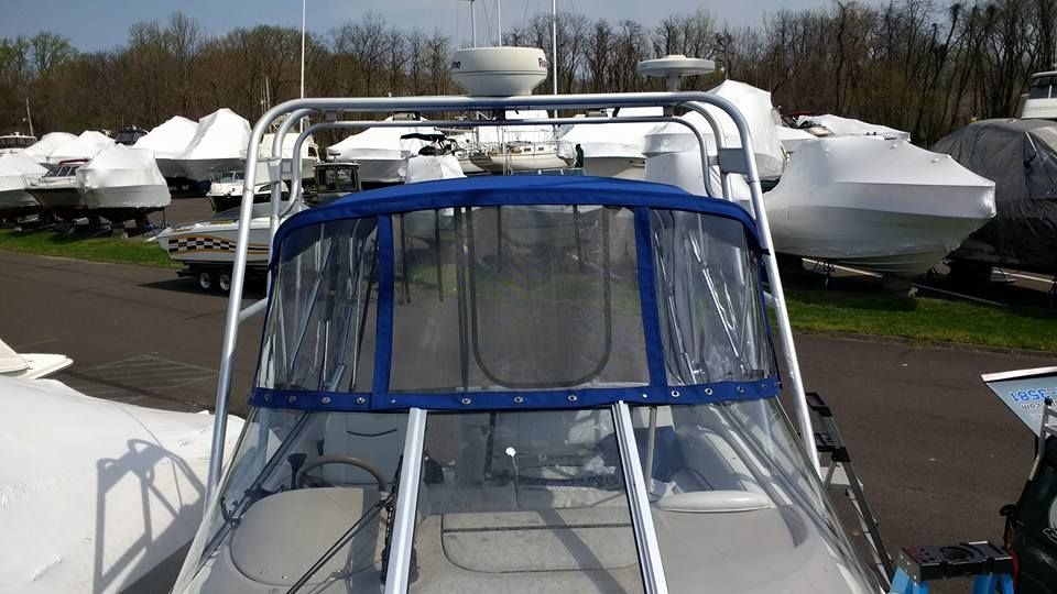 Boat cockpit with blue canvas enclosure in a marina, surrounded by covered boats.