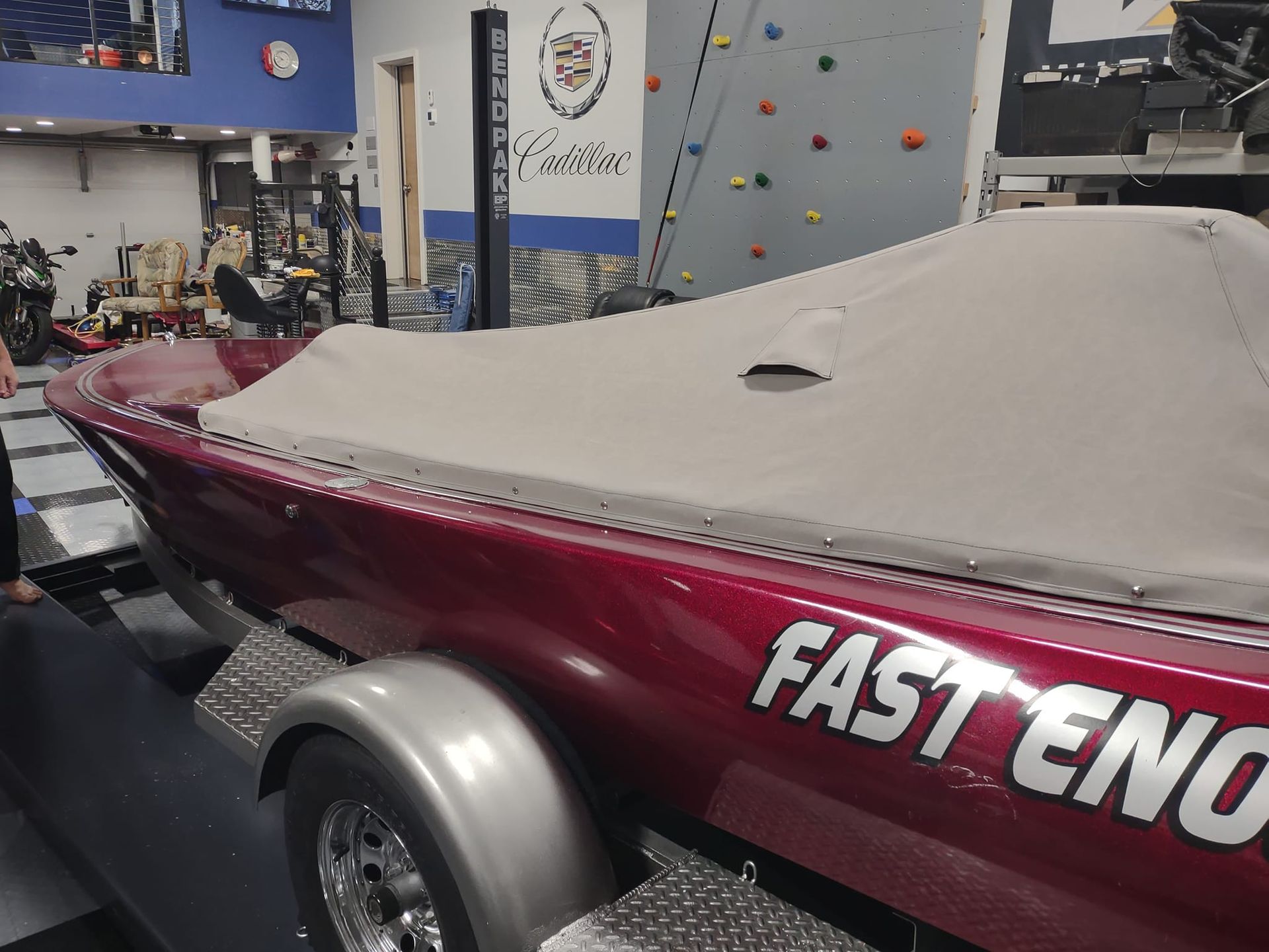Maroon speedboat with gray cover in a workshop, labeled “FAST ENOUGH” on the side.
