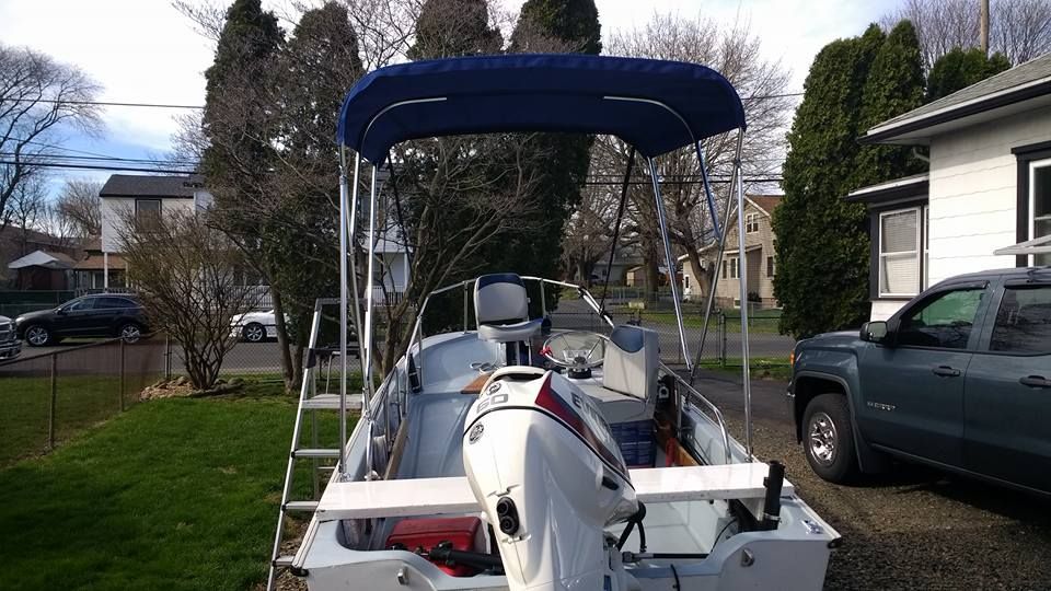 White motorboat with blue canopy parked in a driveway beside a house and truck.