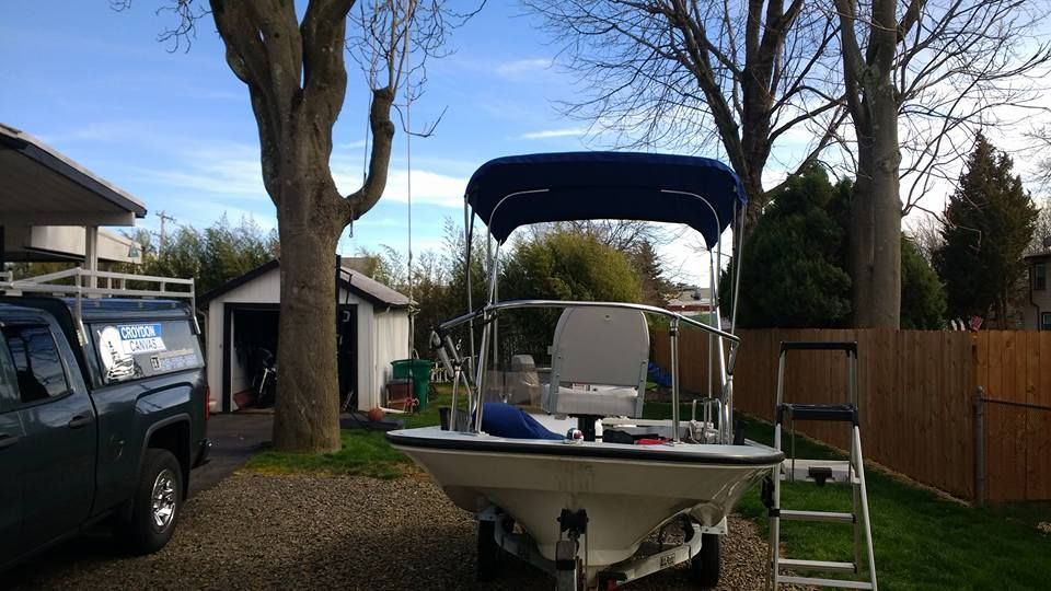 Small boat with blue canopy in a backyard beside a tree, fence, and parked truck