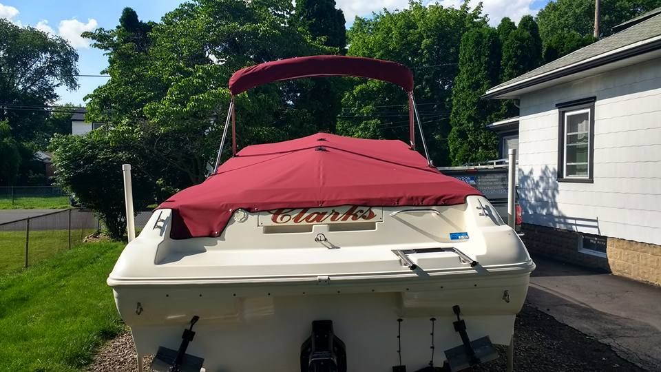 White boat with a red cover parked beside a house on a sunny driveway