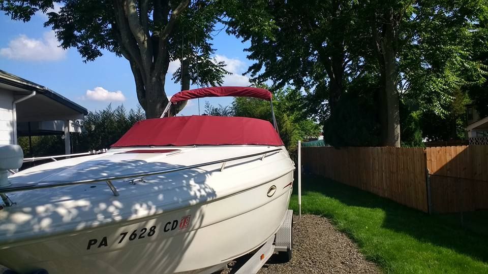 White boat with red canopy on a trailer in a driveway beside a lawn and wooden fence