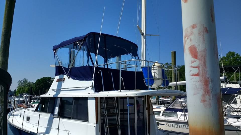 White boat with blue canopy docked at a marina, with other boats and a rust-streaked pole in the foreground