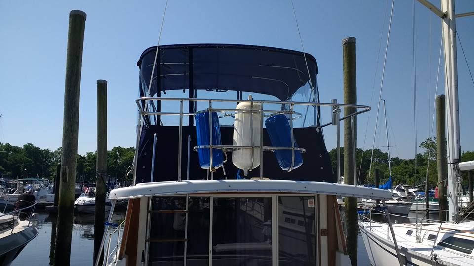 Boat stern docked in marina, with blue canvas canopy and white railings.