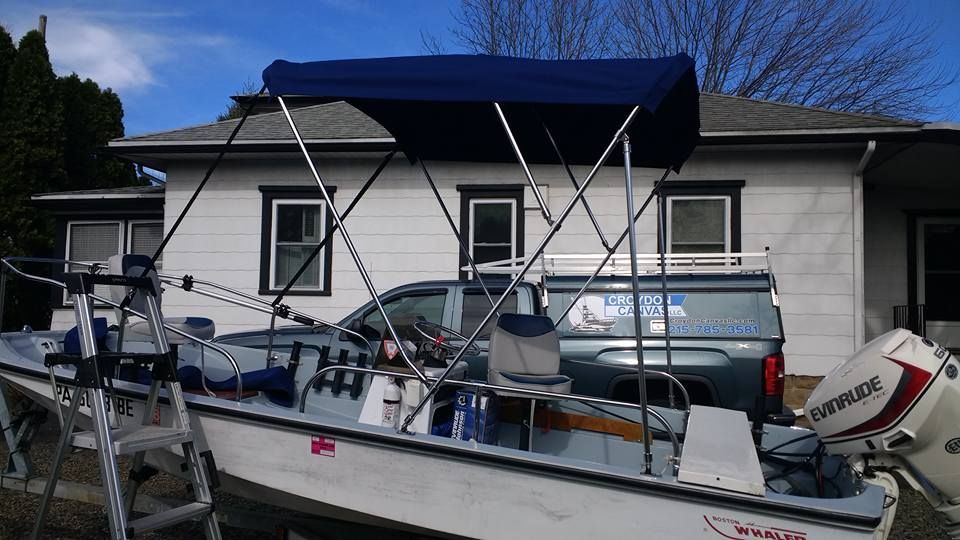 White motorboat with blue canopy and outboard engine parked beside a house in a driveway