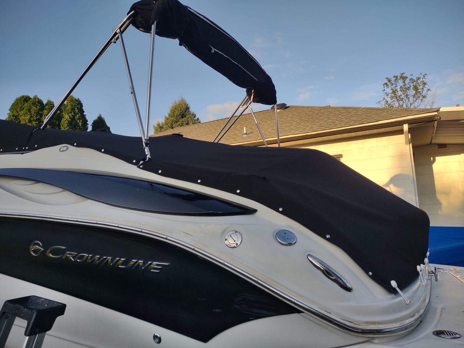 White and black boat with raised canopy docked beside a house under a clear blue sky