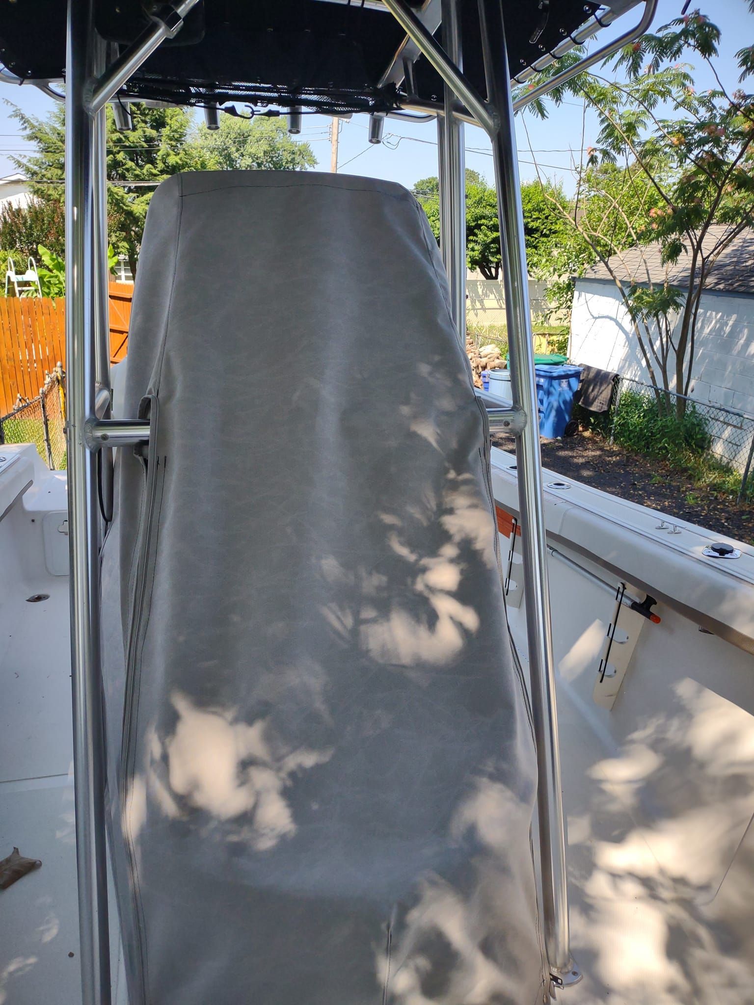 Covered boat seat framed by metal supports on a sunny deck, with trees and railing in the background