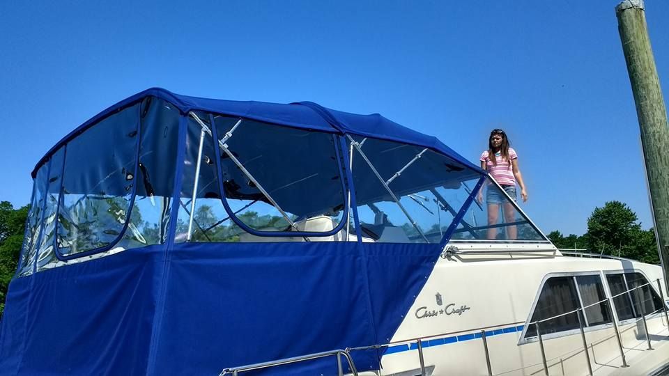 Blue-covered boat on the water with a person standing on the deck under a clear sky