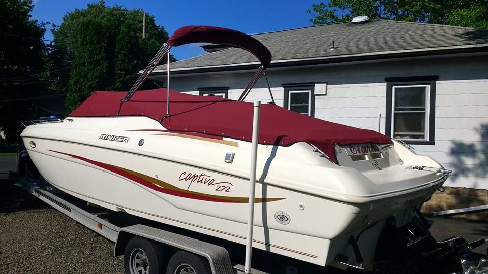 White and red motorboat on a trailer beside a white building, with a red canopy raised.