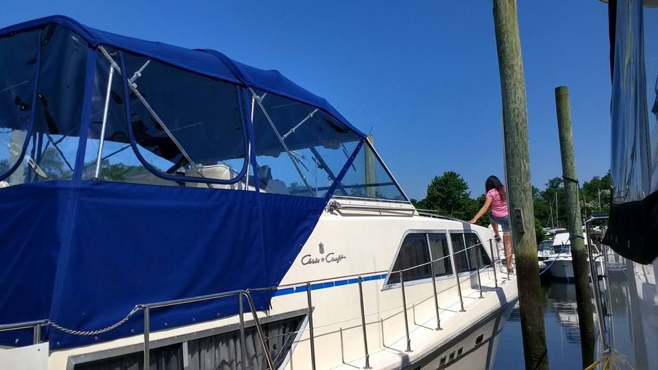White boat with blue canopy docked at a marina, with a person standing on deck under a clear sky.