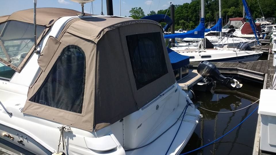 Boat with beige canvas canopy docked at a marina, with sailboats and blue sky in the background
