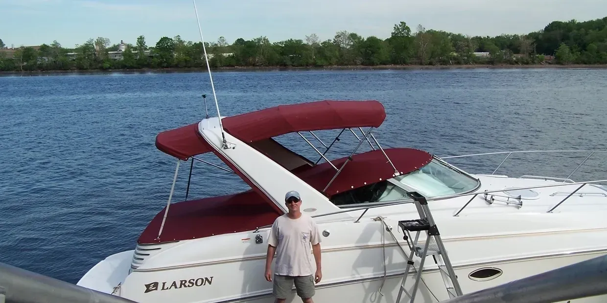 White and burgundy speedboat on a lake, with a person standing by the dock side.