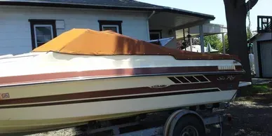 White and brown boat on a trailer beside a house, covered with an orange tarp