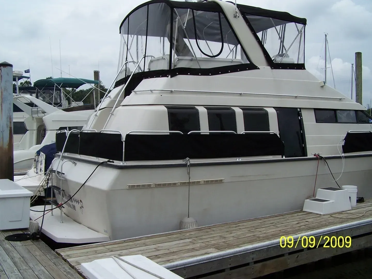 White yacht docked at a marina, with black canopy and windows on a wooden pier