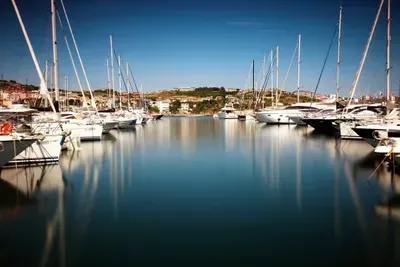 Yachts moored in a calm marina under a clear sky, with reflections on the water