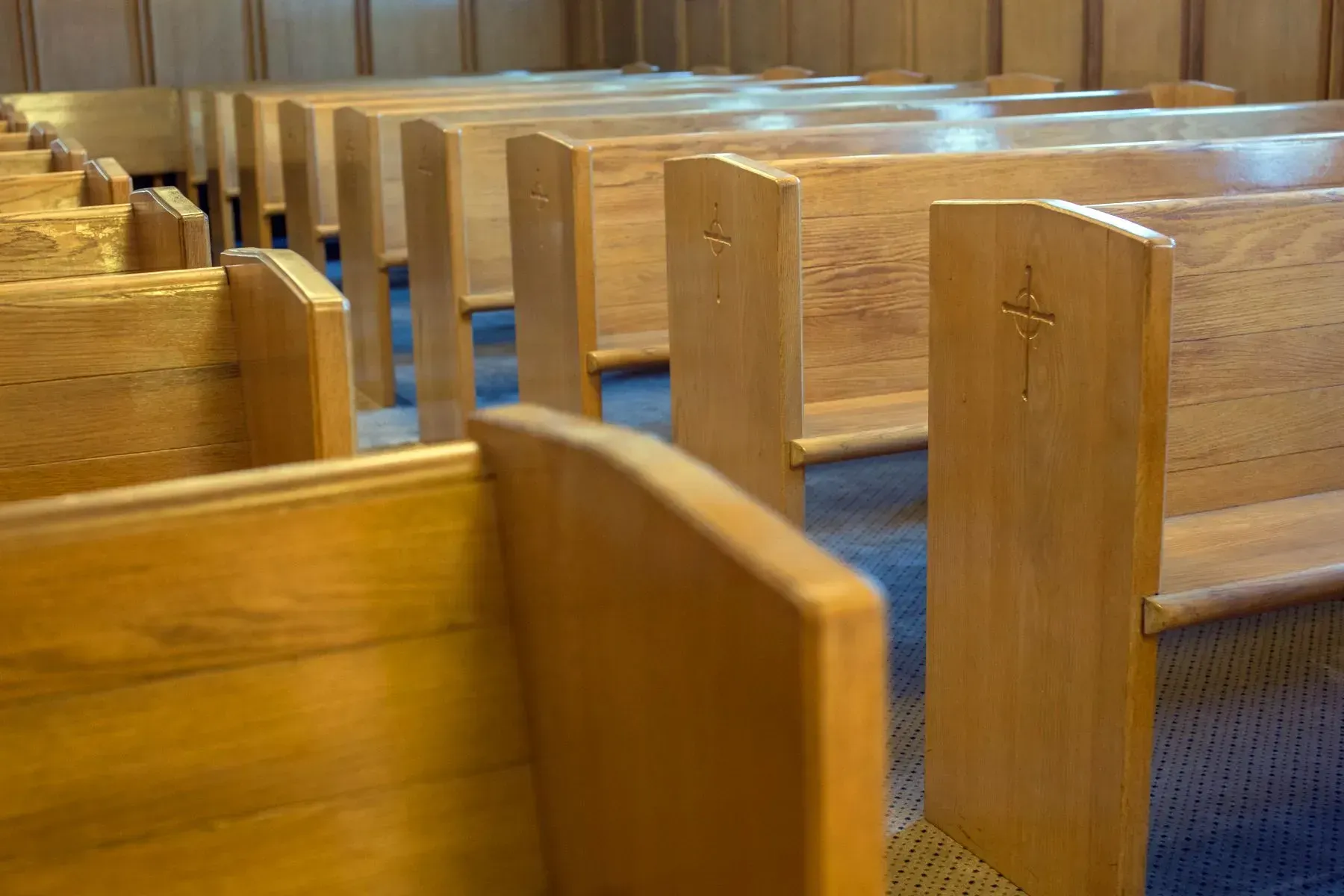 Wooden church pews with blue carpeted aisles in a quiet interior.