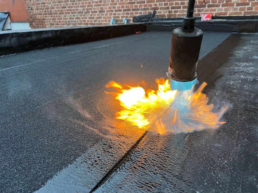 A rooftop torch flares beside a metal pipe on a wet black roof.