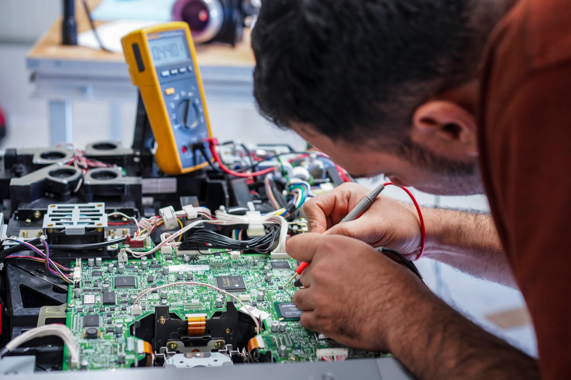 Ein Mann arbeitet mit einem Multimeter an einer Hauptplatine von einem Projektor.