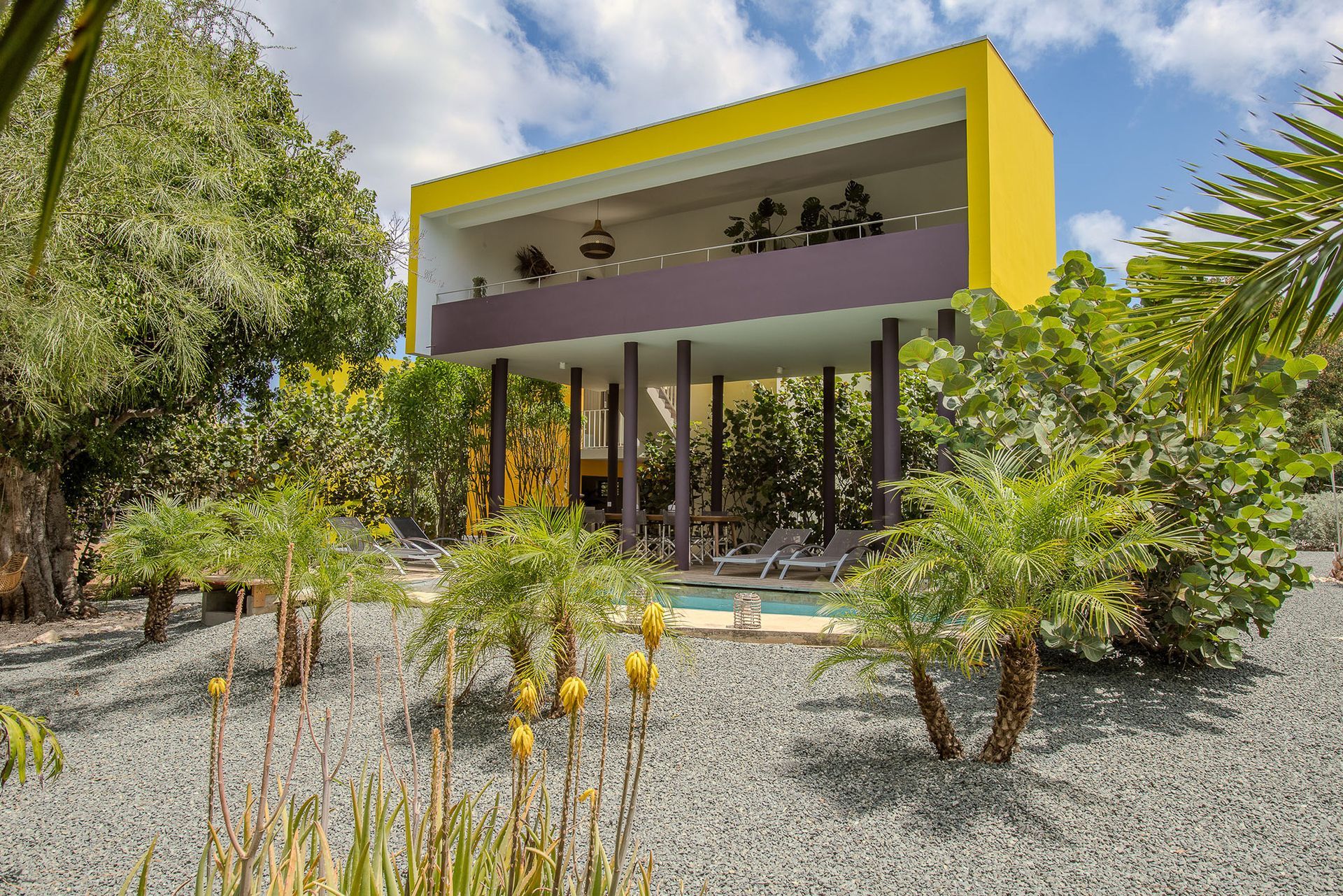 Een modern geel en paars huis op palen met een klein zwembad in de tuin.