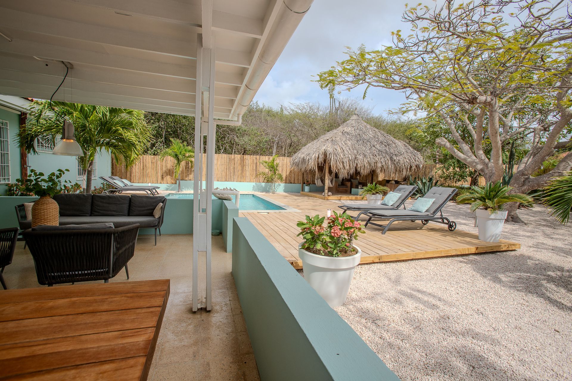 Buitenpatio met zitgelegenheid, zwembad en cabana met rieten dak.
