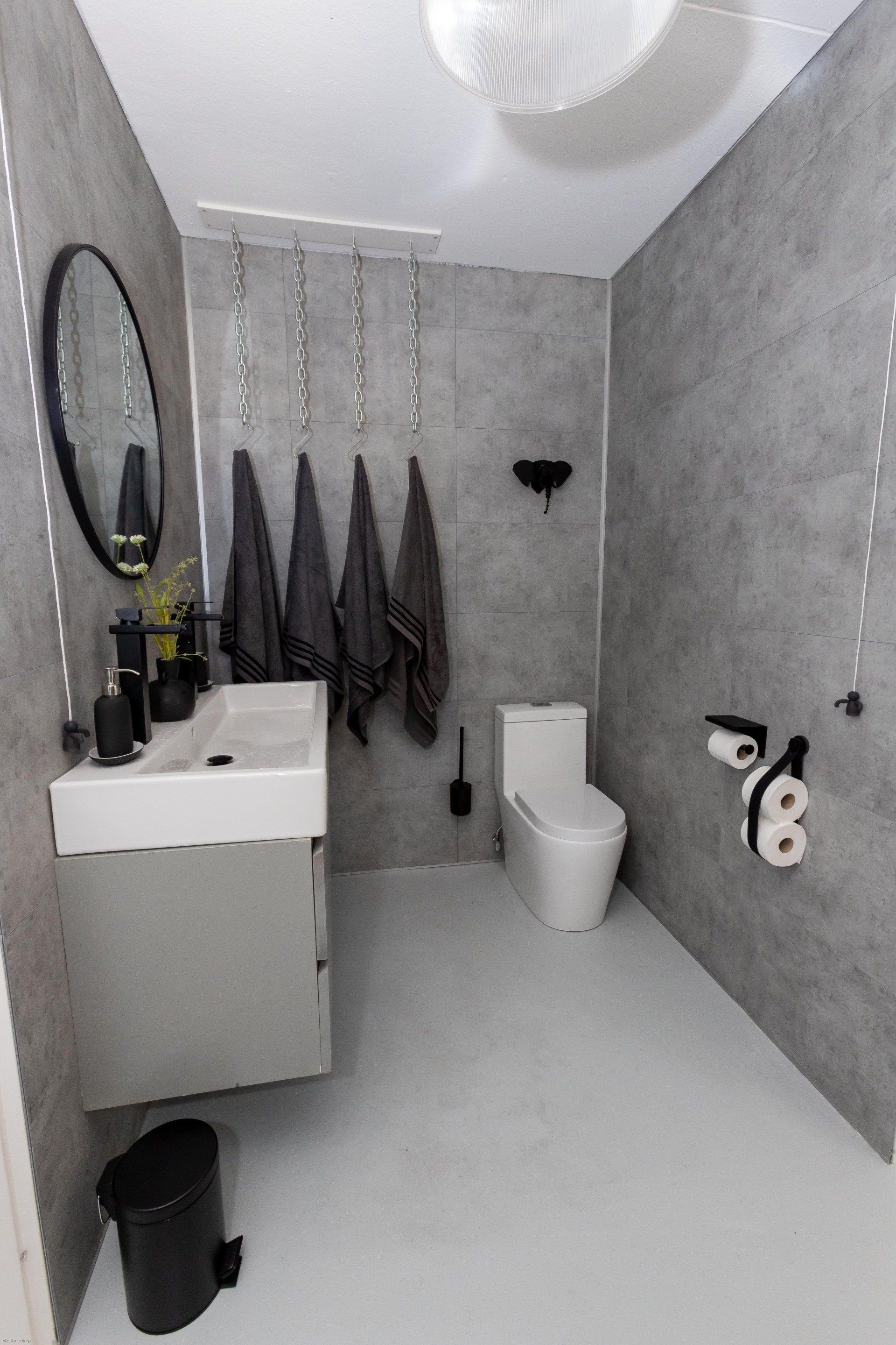 Moderne grijze badkamer met toilet, wastafel en handdoekenrek.