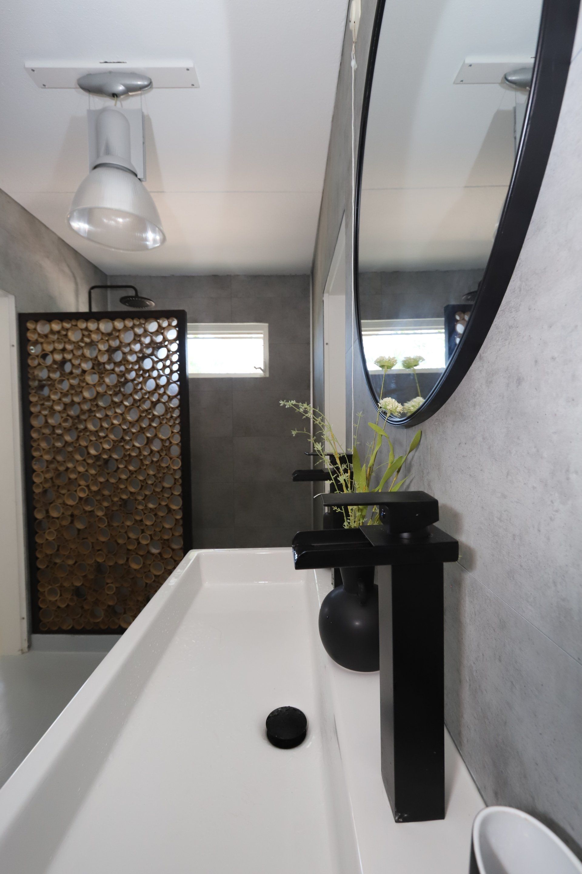 Moderne badkamer met een lange witte wastafel, zwarte kraan, grote spiegel en een accentmuur van hout.