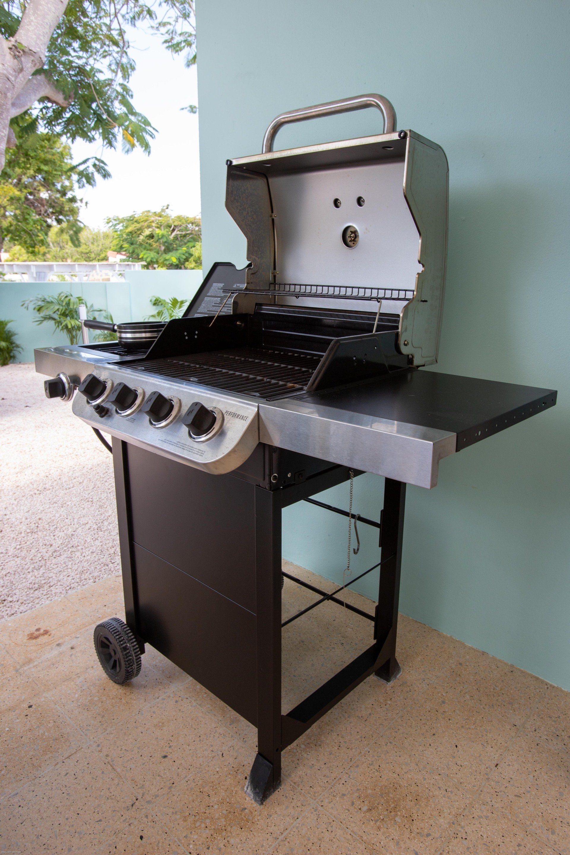 Zwarte gasbarbecue met roestvrijstalen deksel en bijzettafel, geplaatst op een terras.