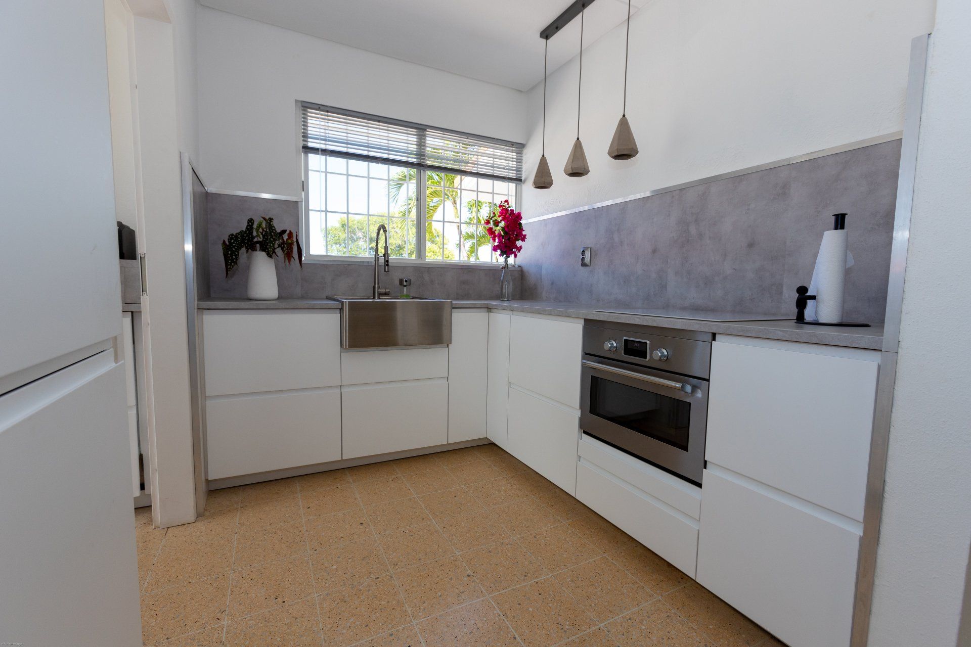 Moderne witte keuken met roestvrijstalen apparatuur, terrazzovloer en raam.