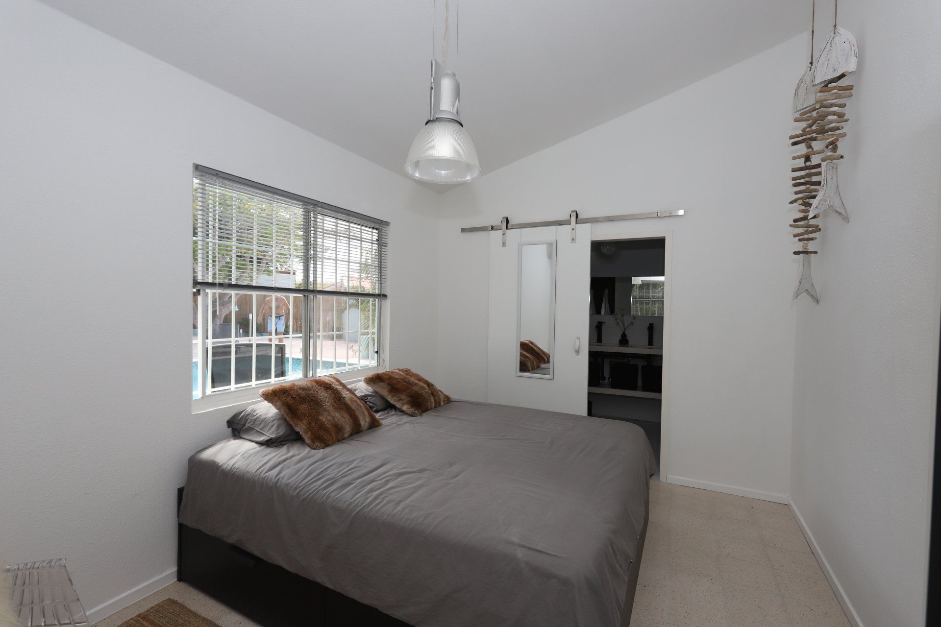 Slaapkamer met bed, raam, schuifdeur, witte muren en hanglamp.